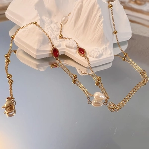 Dettaglio della collana d'oro con gemme rosse e perle barocche su espositore bianco