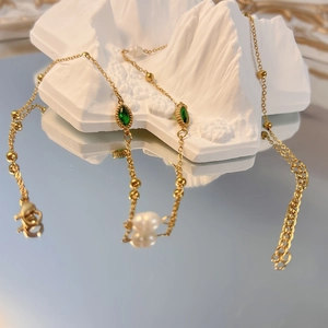 Dettaglio collana dorata con gemme verdi marquise e perle bianche su decorazione in pietra