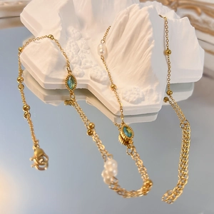 Dettaglio collana vintage dorata con gemme verde acqua e perle su supporto in pietra
