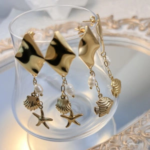 Gold starfish and sea shell drop earrings with pearls hanging on glass edge
