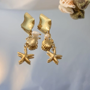 Macro shot of gold stainless steel shell and starfish drop earrings with baroque pearls
