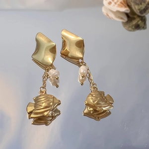 Detail of gold earrings with tropical fish charm and white pearls on mirror surface