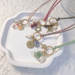 Braided rope necklace with sun eye charms, natural stones and pearls on white tray