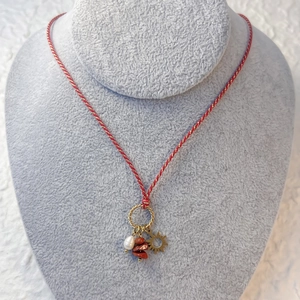 Detail of woven rope necklace featuring a sun pendant, natural stones, and a white pearl