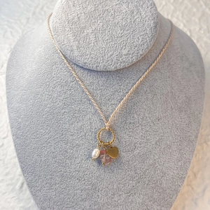 Detailed view of woven cord necklace with pearl, pink gemstone, and gold heart charms