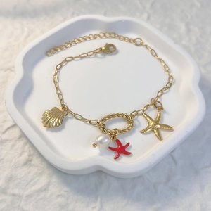 Nahaufnahme des goldenen Ozean-Armbands mit Seesternen und Perlen auf weißem Tablett