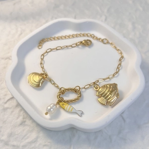 Makroansicht goldener Meeresanhänger mit Fisch, Muschel und Perle an feiner Kette