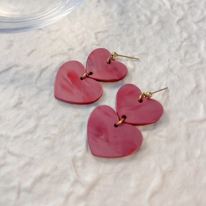 Pink marbled heart drop earrings with gold metal studs on a white textured background