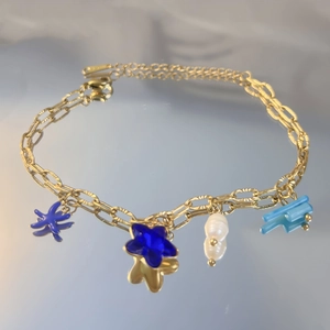 Détail d'un bracelet doré avec pendentifs étoiles, perles et breloques marines