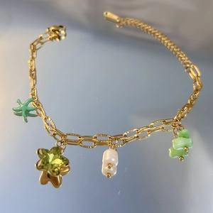 Détail du bracelet chaîne dorée avec pendentif étoile, perle, cristal et pierres vertes