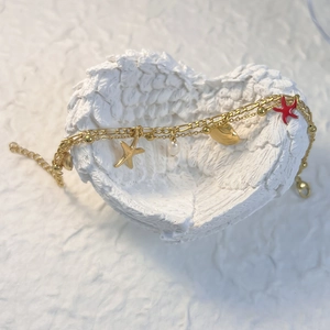 Détail du bracelet doré double rang avec étoile de mer et perles sur plateau décoratif