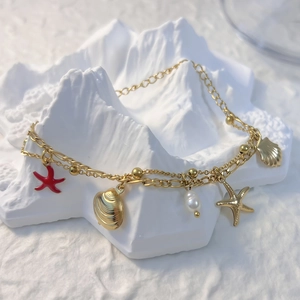 Détail de pendentifs étoile de mer et coquillage dorés sur un bracelet perle double rang