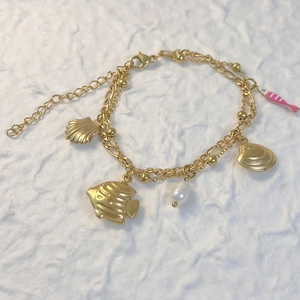 Détail du bracelet doré à deux rangs avec breloques coquillage, étoile de mer et perle
