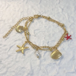 Détail de breloques étoile de mer dorées et perles sur un bracelet double en acier