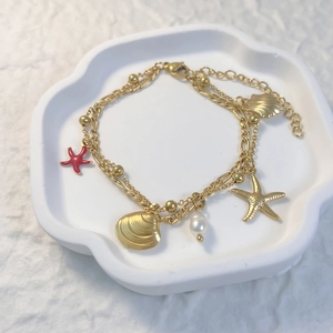 Bracelet double rang doré avec étoile de mer, perle et coquillage sur plateau