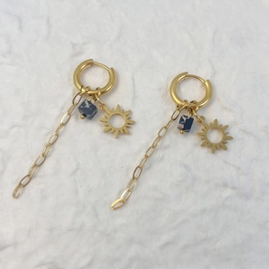 Detail of gold sun-shaped earrings with blue floral beads and long chain tassels