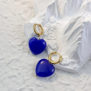 Dettaglio di orecchini a cuore in pietra blu su piedistallo bianco artistico