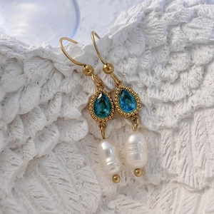 Détail de boucles d'oreilles dorées avec cristaux bleus et perles d'eau douce