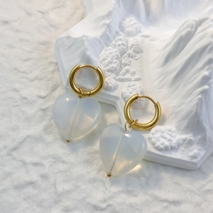 Dettaglio di orecchini a cuore in oro con quarzo opaco su vassoio decorativo