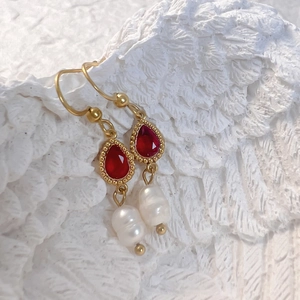 Détail de boucles d'oreilles dorées avec strass rouges et perles d'eau douce baroques