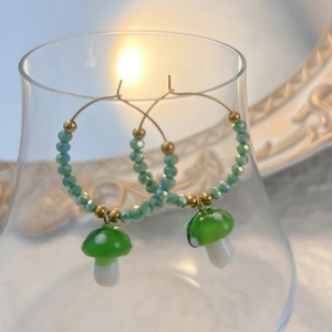 Close-up of glass mushroom drop earrings with green beads hanging on a clear glass