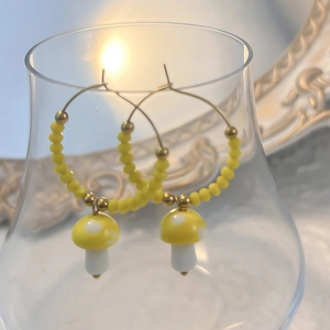 Close-up of yellow polka dot mushroom charm on gold hoop earrings with small beads