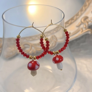 Detail of red polka dot mushroom earring with gold beads on a clear glass rim