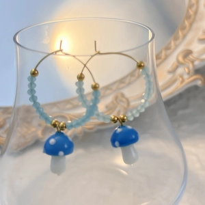Detail of blue polka dot glass mushroom pendant earrings hanging on a transparent glass