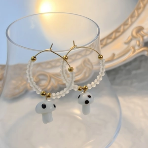 Close-up of cute glass mushroom hoop earrings with white beads on a golden metal ring