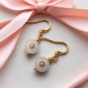 Macro view of pink quartz drop earrings with gold hooks on a white textured background