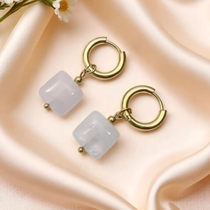 Detail of geometric natural stone earrings with gold hoops on elegant silk fabric