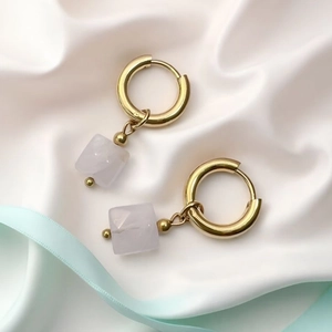 Close-up of geometric gold hoop earrings featuring polished pink quartz stone cubes