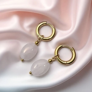 Close-up of gold stainless steel earrings with oval pink quartz charms on satin fabric