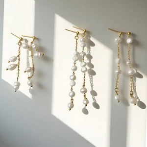 Elegante Goldene Perlenohrringe mit Quasten-Design an einer weißen Wand präsentiert