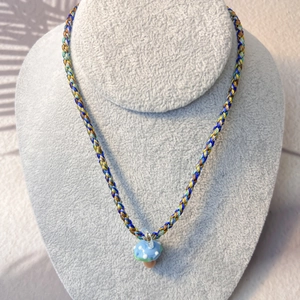 Macro detail of bohemian braided necklace with a blue spotted mushroom pendant