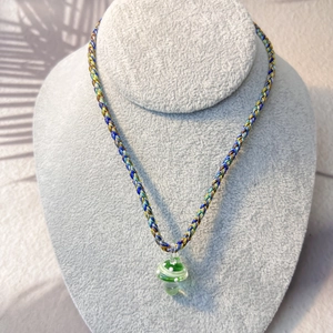 Macro detail of a green glass mushroom pendant on a colorful hand-woven cord necklace