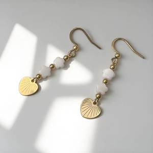 Gold earrings with white star beads and heart pendants shown in soft natural sunlight
