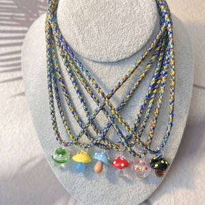 Colorful handmade glass mushroom pendant necklaces on a grey velvet jewelry display stand