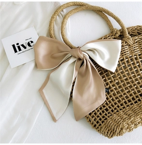 Detail of a two-tone satin ribbon scarf tied as an elegant bow on a woven straw handle
