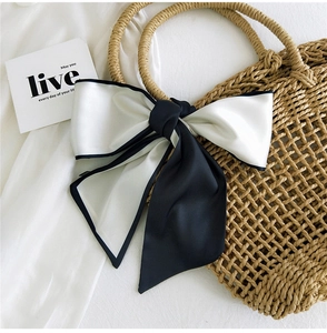 Detail of black and white silk ribbon bow tied on a straw handbag handle accessory