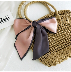 Detail of pink and taupe ribbon scarf tied in a bow on a woven bag with refined edges
