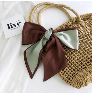 Detail of two-tone satin scarf bow in coffee and green on a straw tote bag