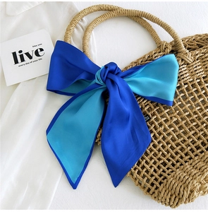 Close-up of a blue two-tone silk scarf tied in a bow on a straw bag handle