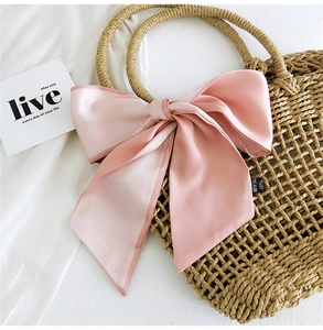 Pink satin bow accessory tied on a straw bag showing smooth texture and elegant detail