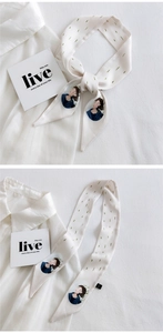 Detail of cream silk twilly scarf featuring green leaf patterns and cartoon girl illustration
