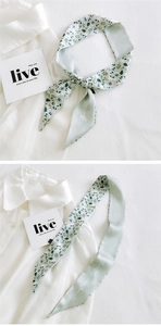 Detail of light green floral skinny scarf tied as a bow on a white collared shirt