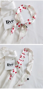 Detailed view of cream silk scarf with red cherry prints tied on a white shirt