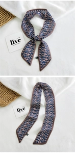 Detail of a floral print narrow silk twilly scarf tied and draped on a white textured background