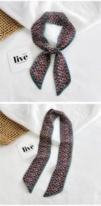 Detail of teal narrow silk scarf with red berry pattern tied and laid flat on fabric