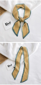 Detailed shot of yellow floral twilly scarf with blue trim and smooth silk-like texture